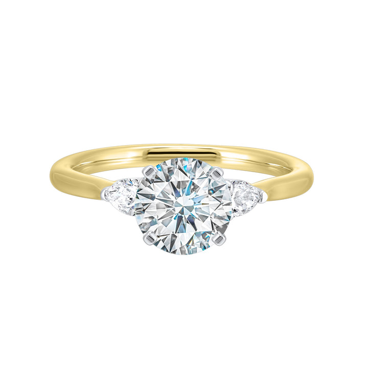 Stunning engagement ring features a round brilliant cut diamond in the center of a three stone setting, adorned on either side by a smaller pear diamond set on the tapered shank.