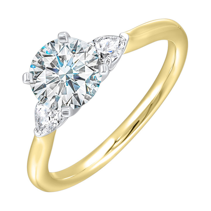 Stunning engagement ring features a round brilliant cut diamond in the center of a three stone setting, adorned on either side by a smaller pear diamond set on the tapered shank.