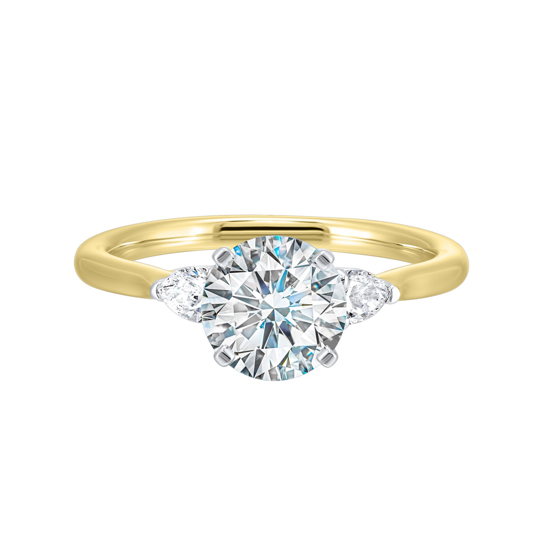 Stunning engagement ring features a round brilliant cut diamond in the center of a three stone setting,  adorned on either side by a smaller pear diamond set on the tapered shank.