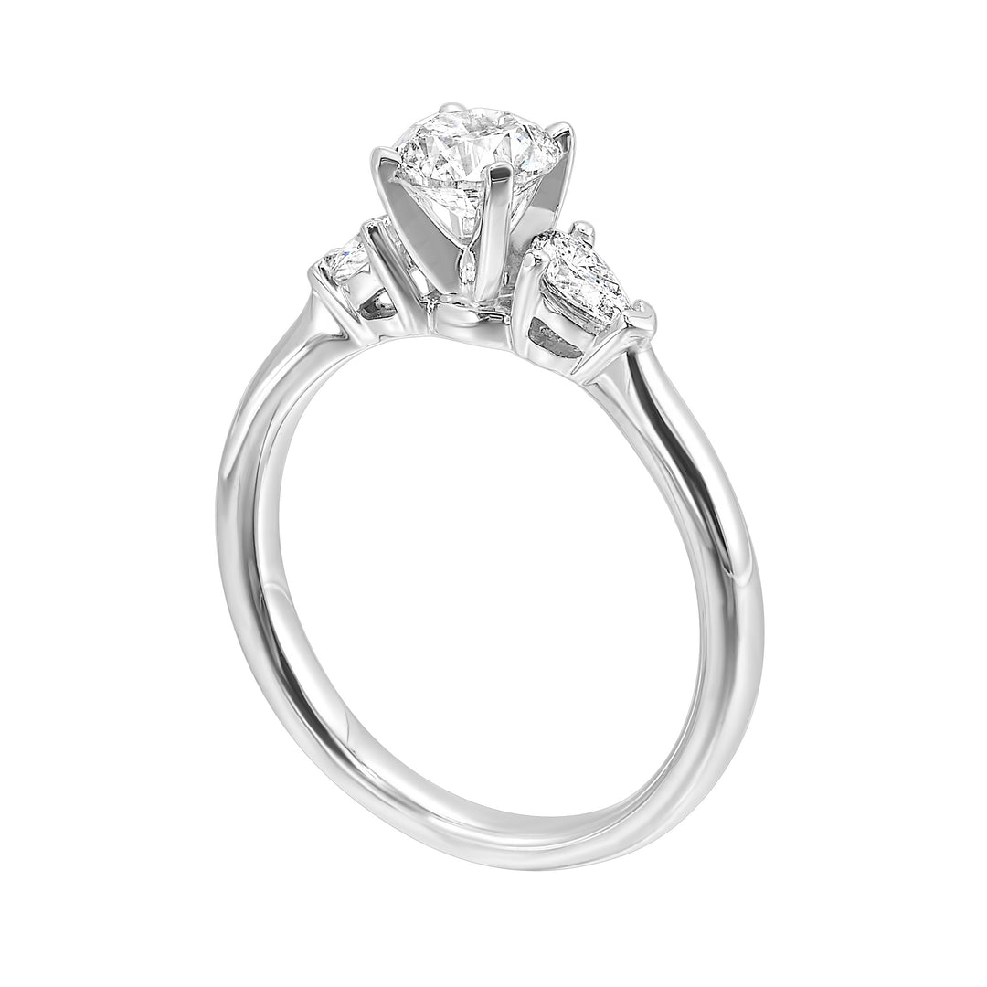 Stunning engagement ring features a round brilliant cut diamond in the center of a three stone setting, adorned on either side by a smaller pear diamond set on the tapered shank.