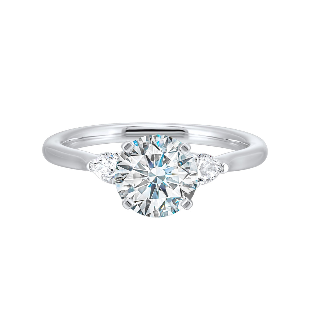 Stunning engagement ring features a round brilliant cut diamond in the center of a three stone setting,  adorned on either side by a smaller pear diamond set on the tapered shank.