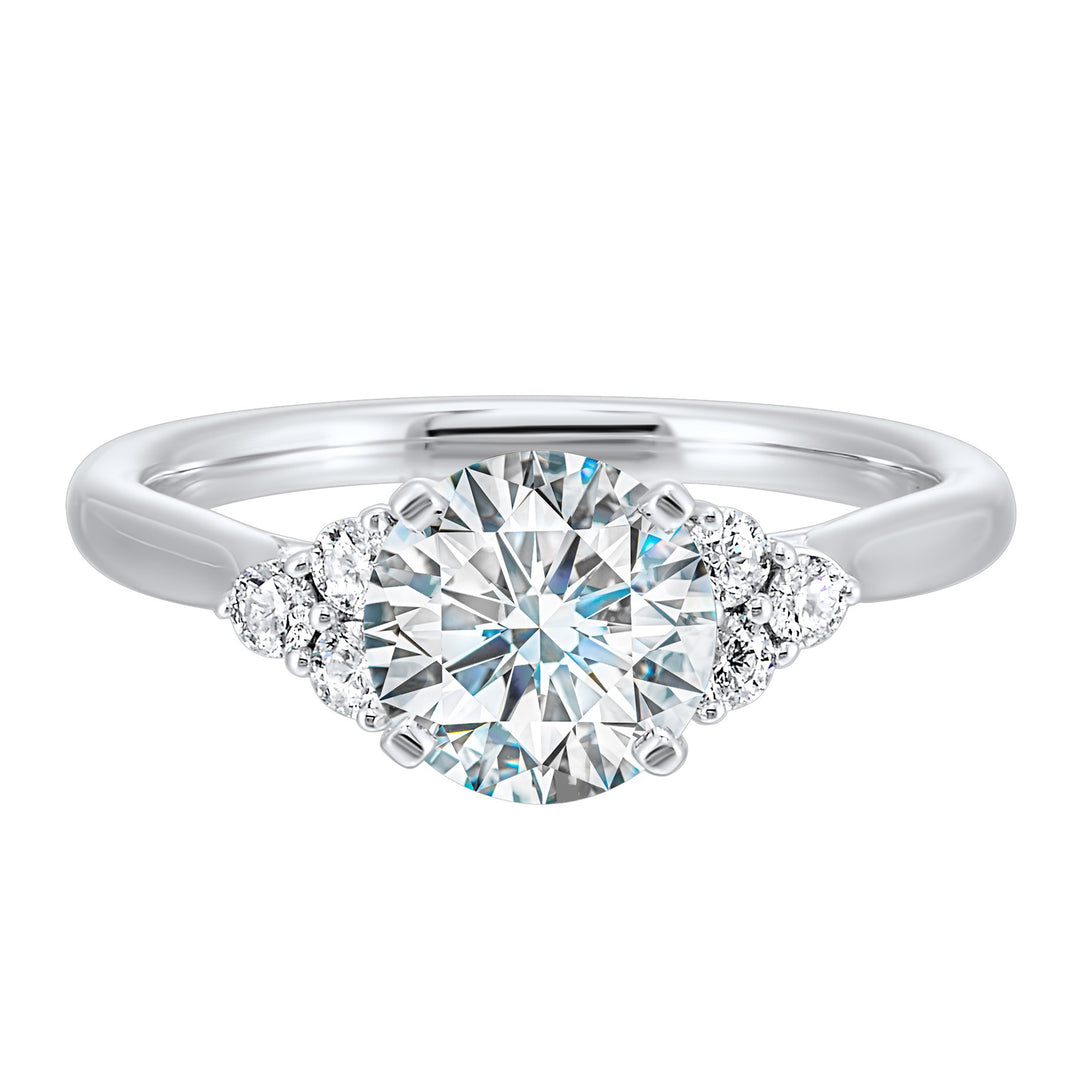 Three stone ring features a trinity of diamonds on either side, focusing the round solitaire at center, is a symbol of everlasting love.