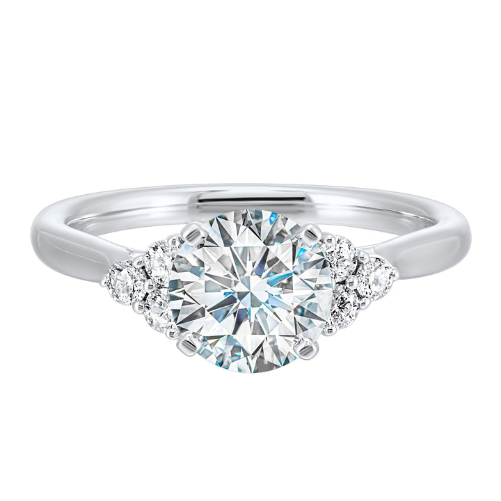Three stone ring features a trinity of diamonds on either side, focusing the round solitaire at center, is a symbol of everlasting love.