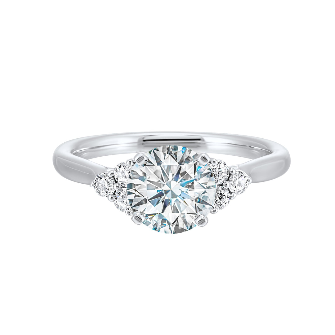 Three stone ring features a trinity of diamonds on either side, focusing the round solitaire at center, is a symbol of everlasting love.
