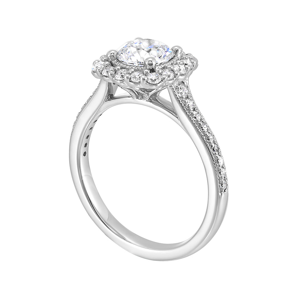 This romantic engagement ring features a round solitare with milgrain details adorned with a delicate cushion style diamond halo and a thin pave band.