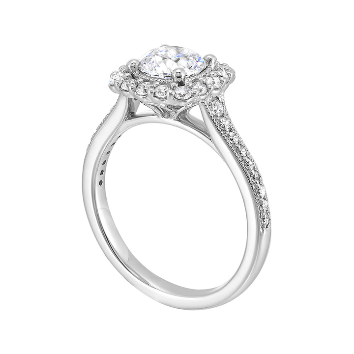 This romantic engagement ring features a round solitare with milgrain details adorned with a delicate cushion style diamond halo and a thin pave band.
